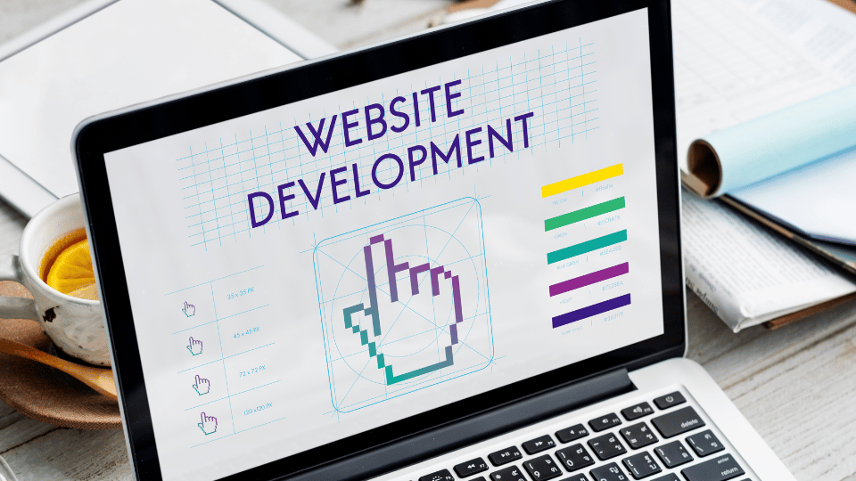 Laptop screen displaying "WEBSITE DEVELOPMENT" with design elements, indicating web design work.