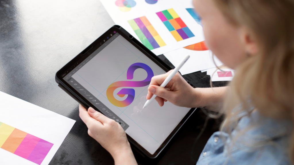 Female designer in Malaysia creating a logo on a tablet, surrounded by color swatches.